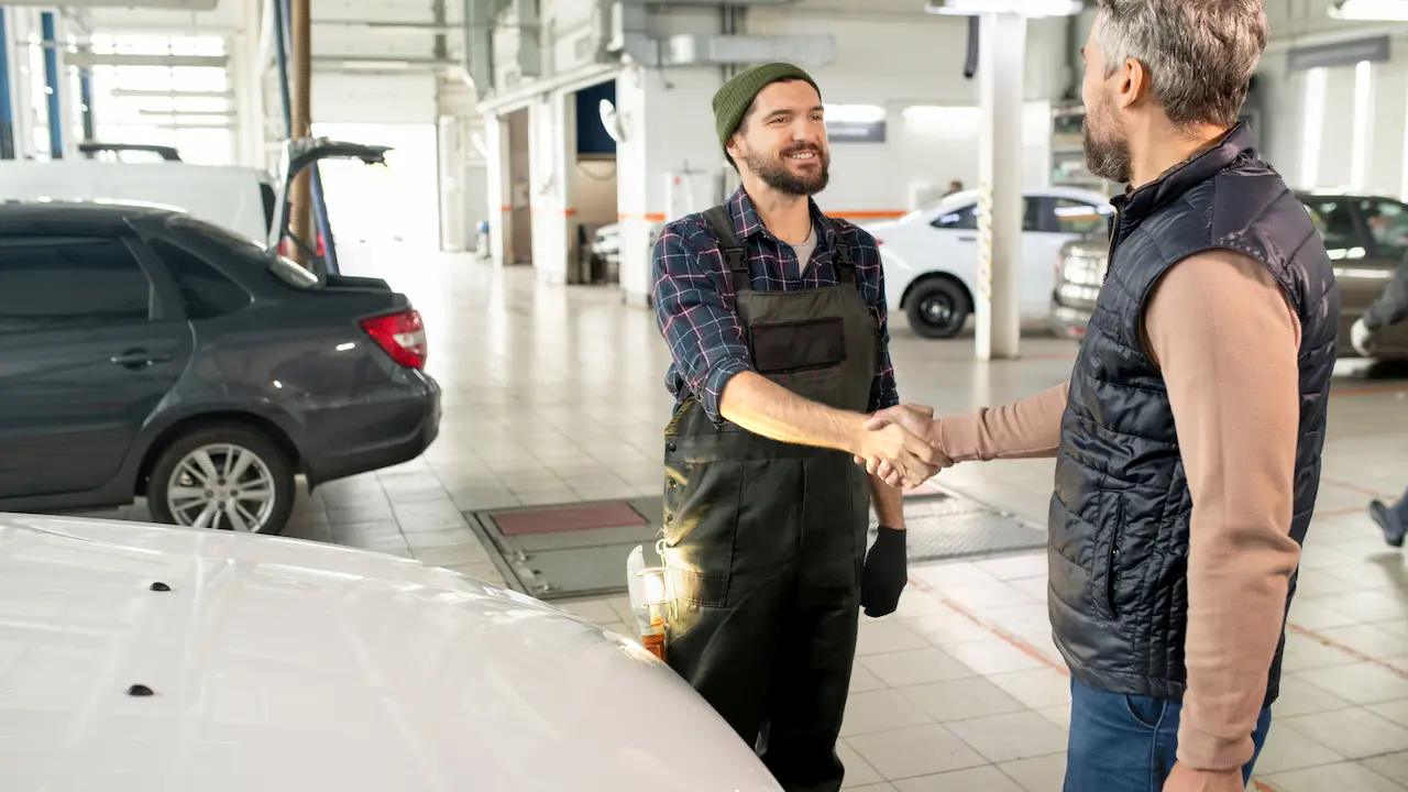 A mechanic and a customer shaking hands inside a garage.
